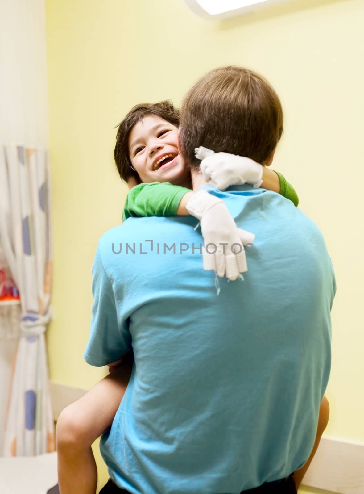 Little boy with cerebral palsy in doctor's office, laughing with his father