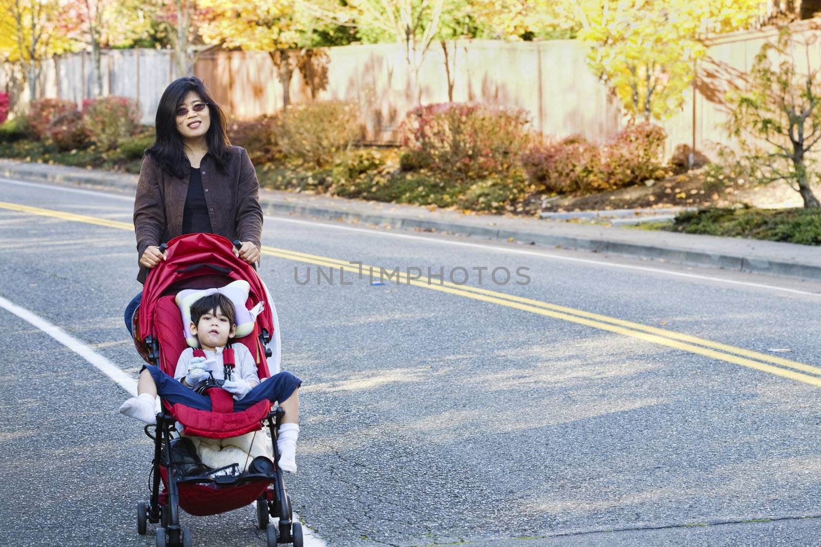 Mother walking with her disabled son in stroller outdoors