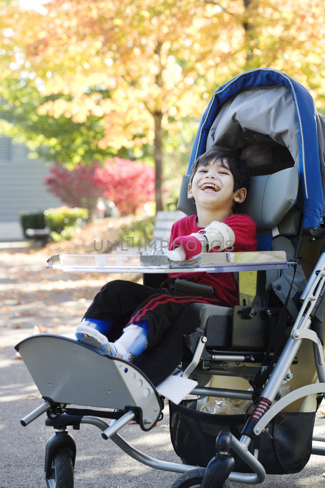 Disabled boy with cerebral palsy in medical stroller enjoying an autumn day outdoors at the park