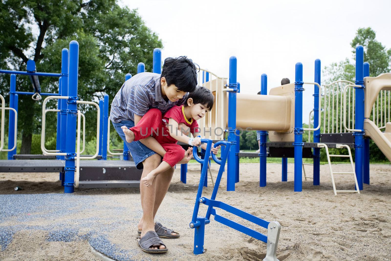 Older brother helping disabled sibling play at playground