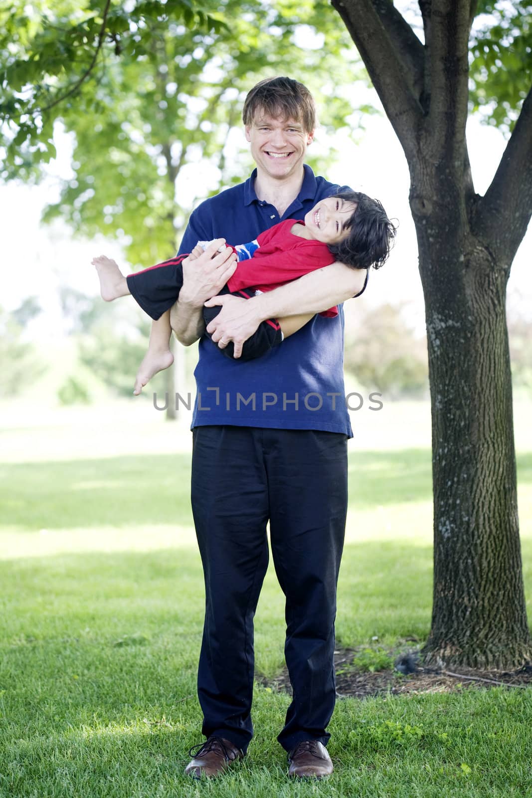 Father holding disabled son outdoors by jarenwicklund