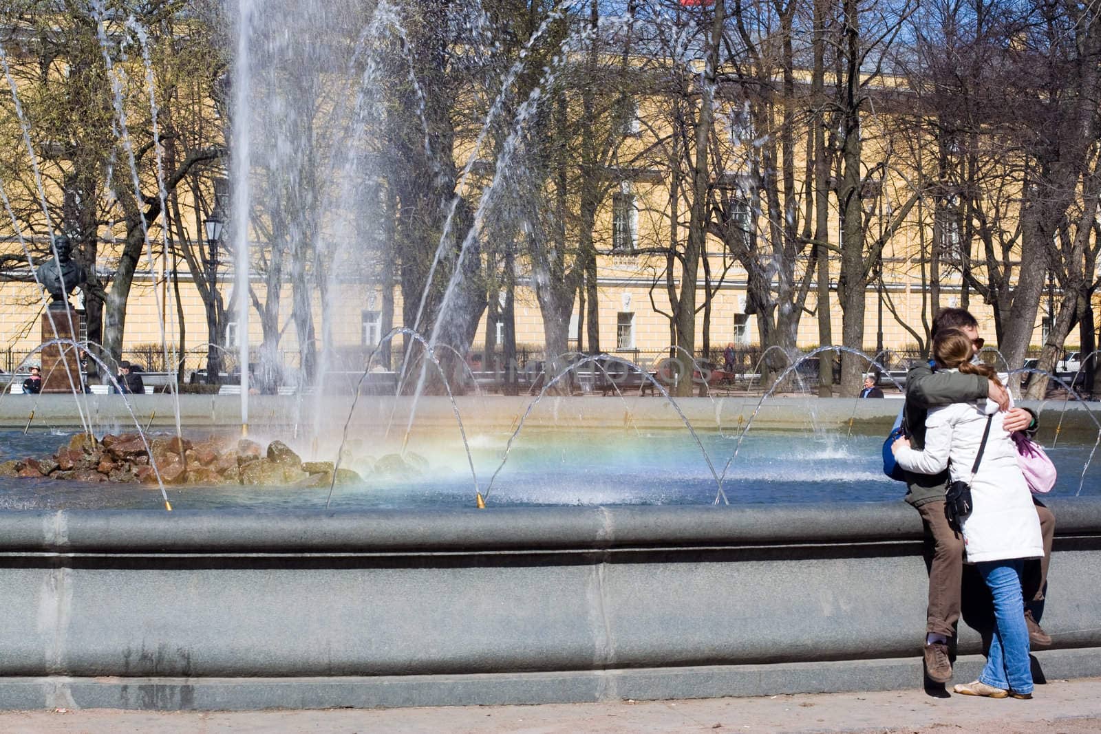 Fountain with rainbow and young pair at front plane