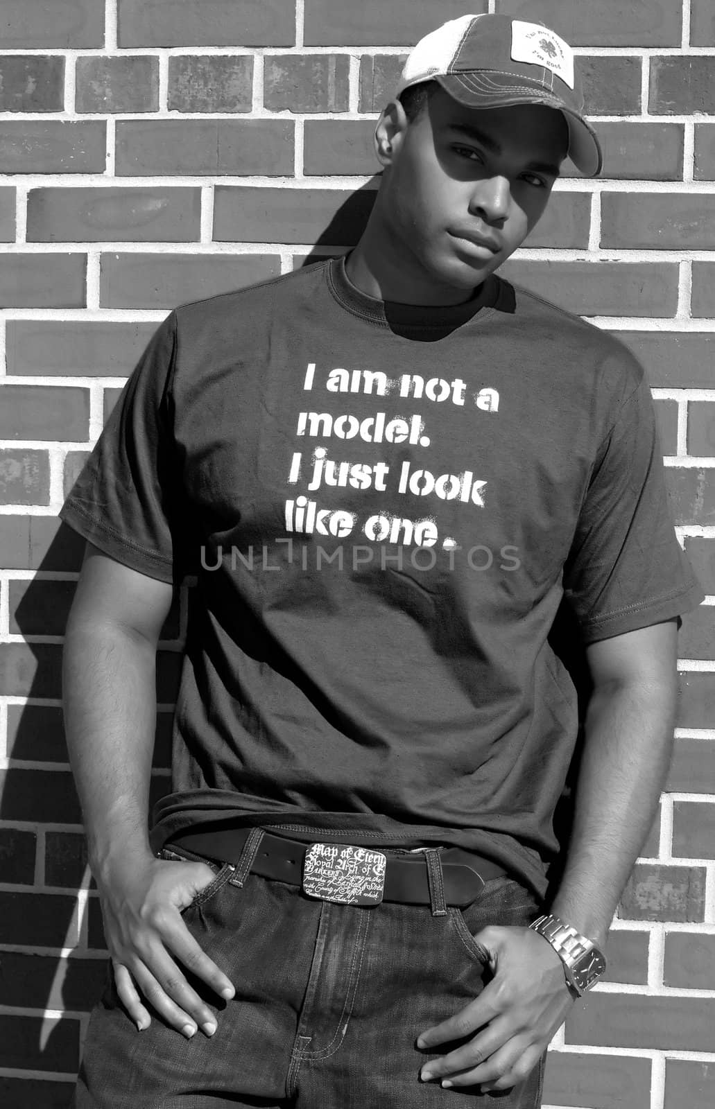 Attractive young African American male playing posing in a t-shirt and jeans against a brick wall.