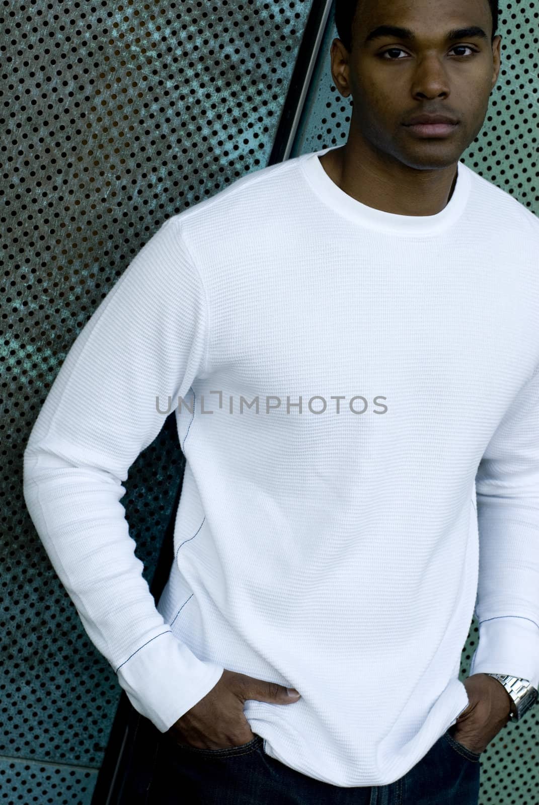 Attractive young African American male playing posing in a white t-shirt and jeans against a mesh green wall.