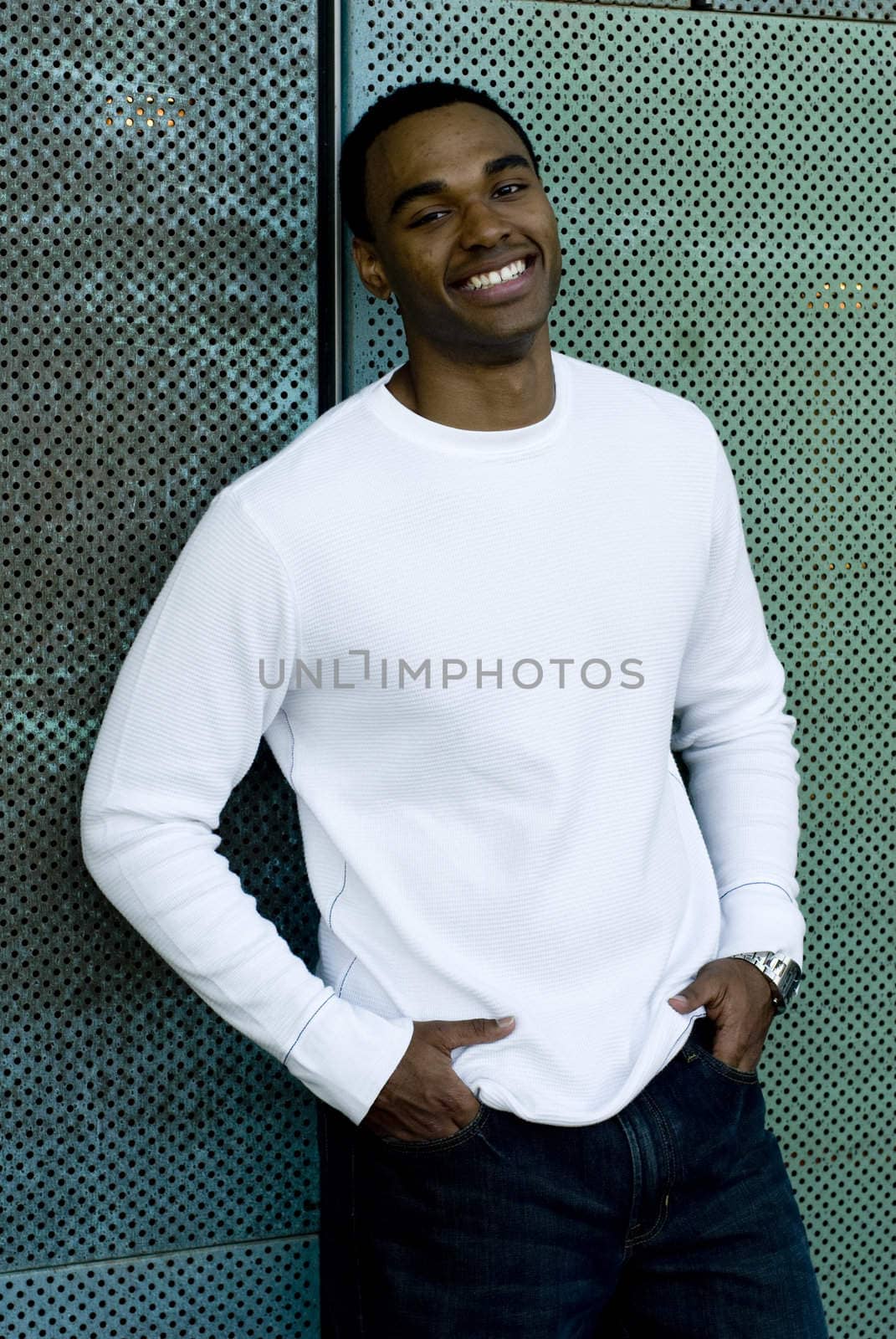 Attractive young African American male playing posing in a white t-shirt and jeans against a mesh green wall.