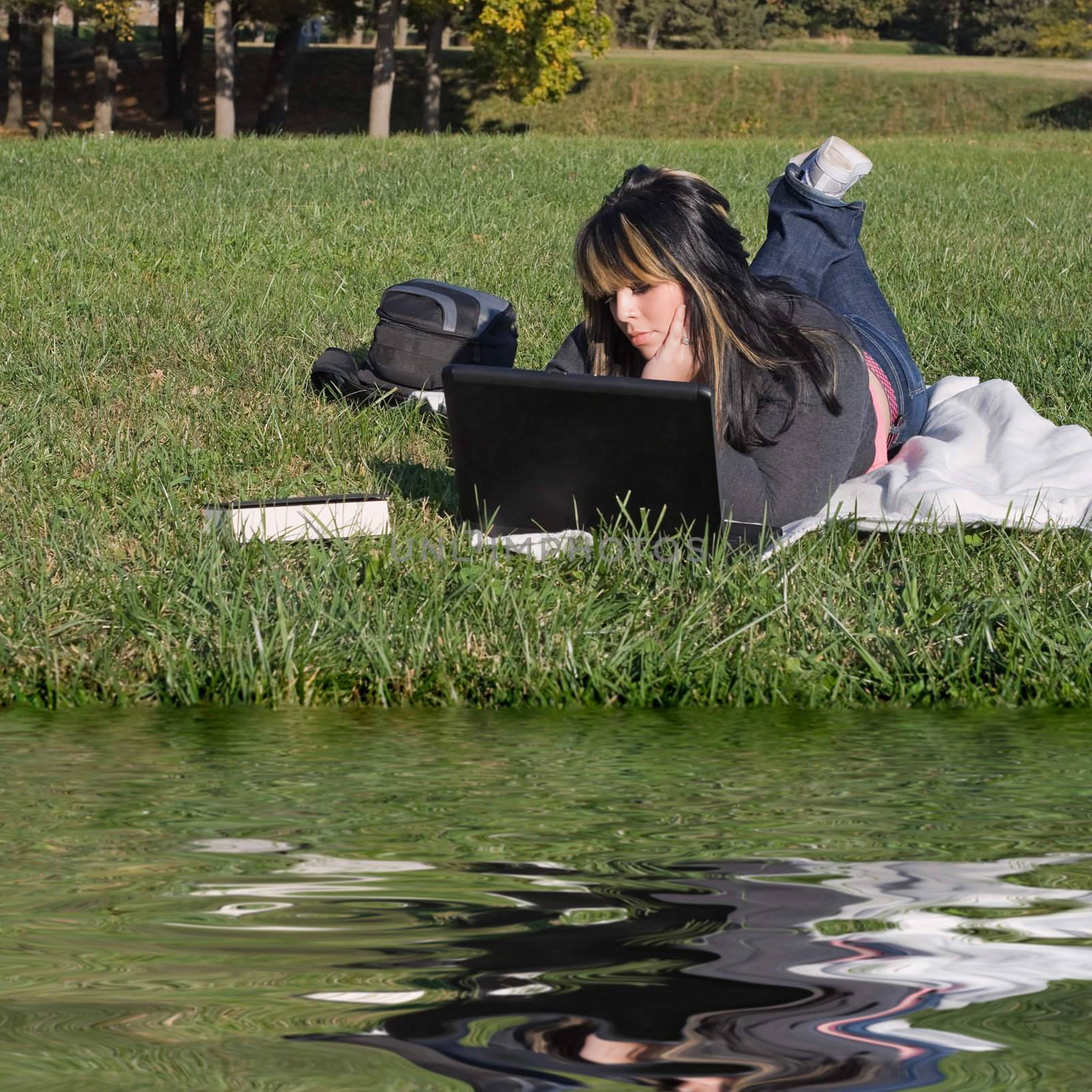 A young student using her laptop computer while laying in the grass on a nice day.