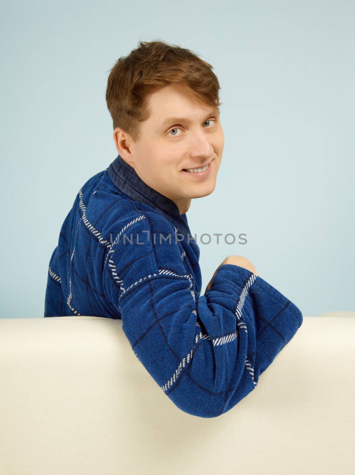 Happy smiling man sitting on a couch in his dressing gown on blue