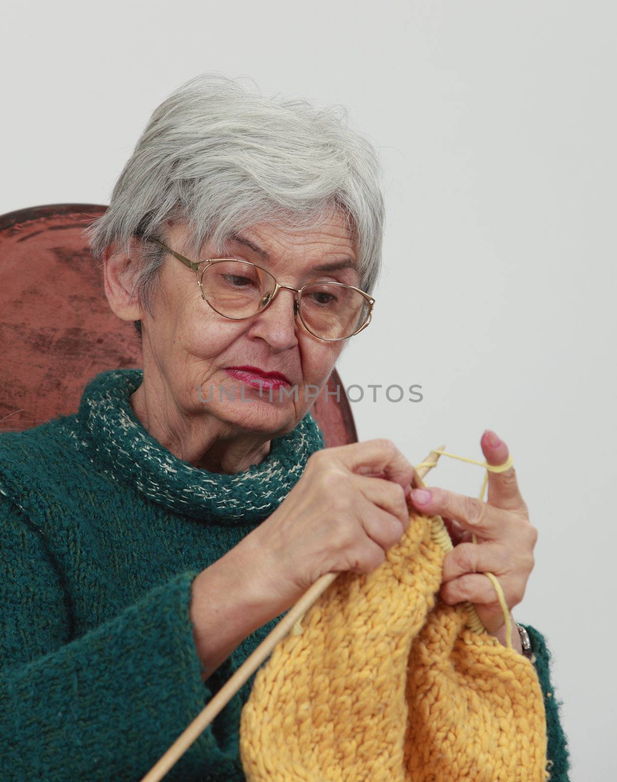 Portrait of an old woman knitting,against a gray background.