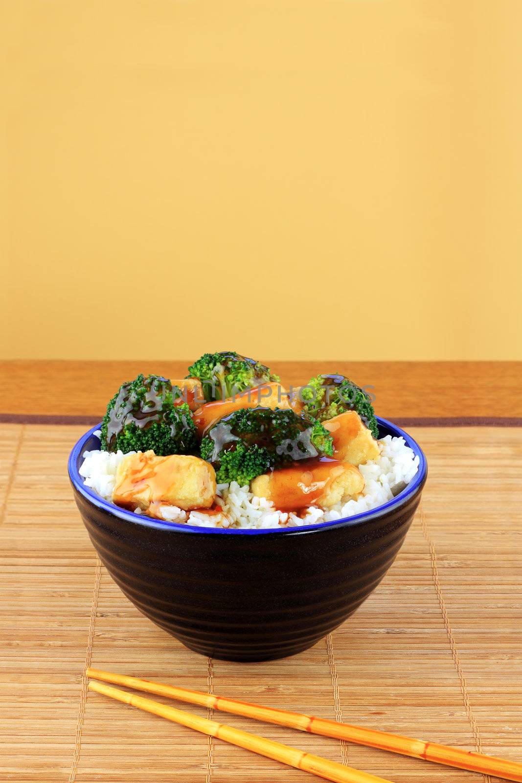 Vegetarian Stir Fry dish of crispy tofu, broccoli and orange sauce with chopsticks.