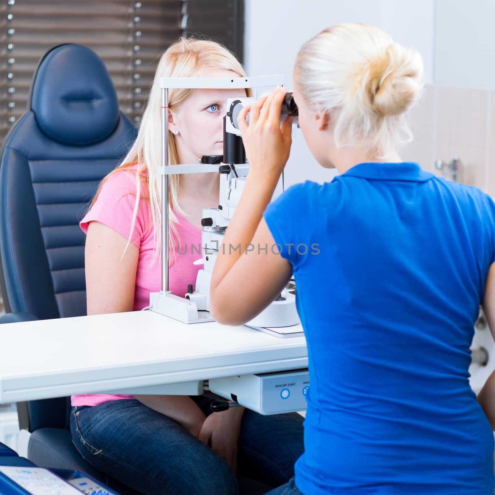 optometry concept - pretty, young female patient having her eyes examined by an eye doctor (color toned image; shallow DOF)