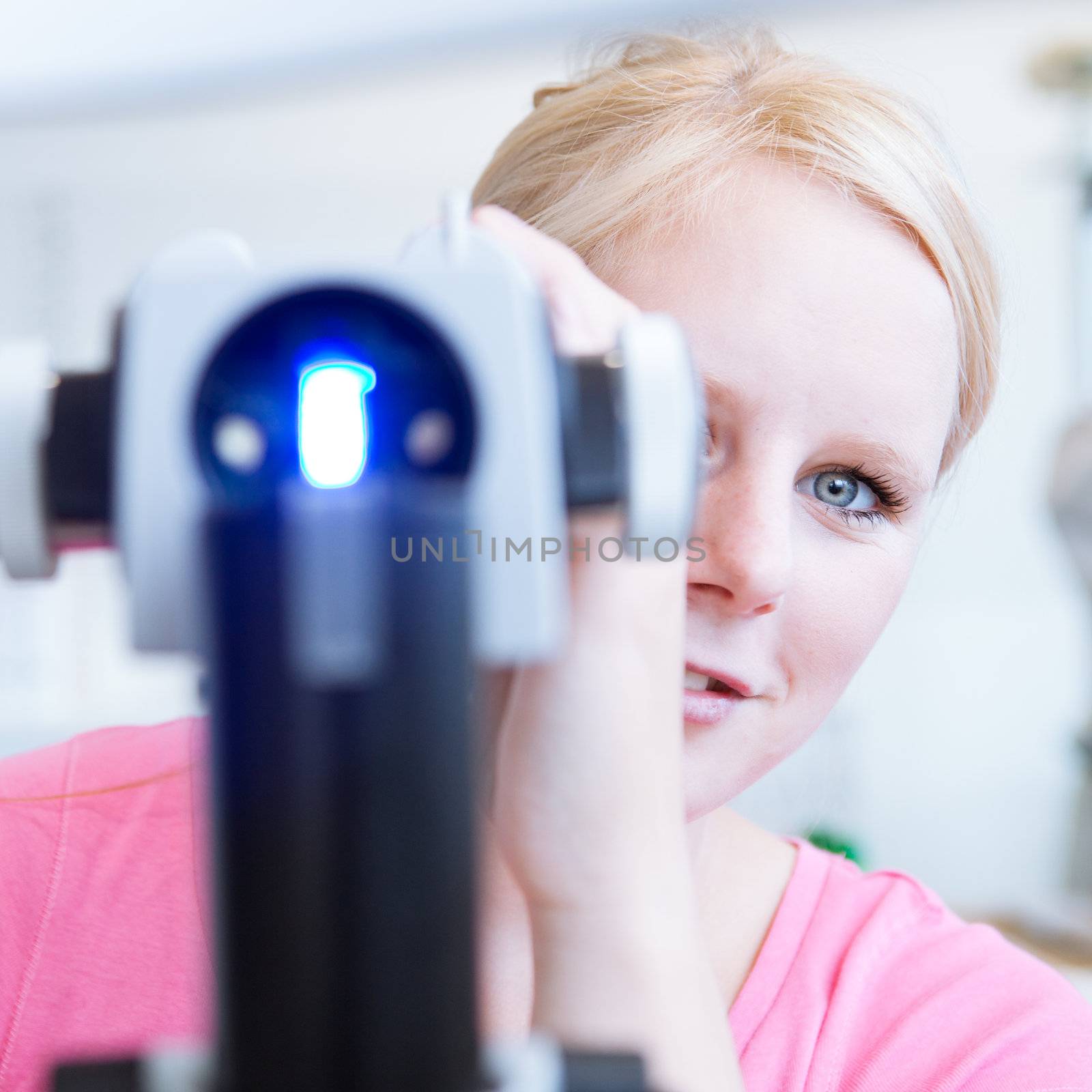 optometry concept - portrait of a young pretty optometrist using slit lamp (color toned image)