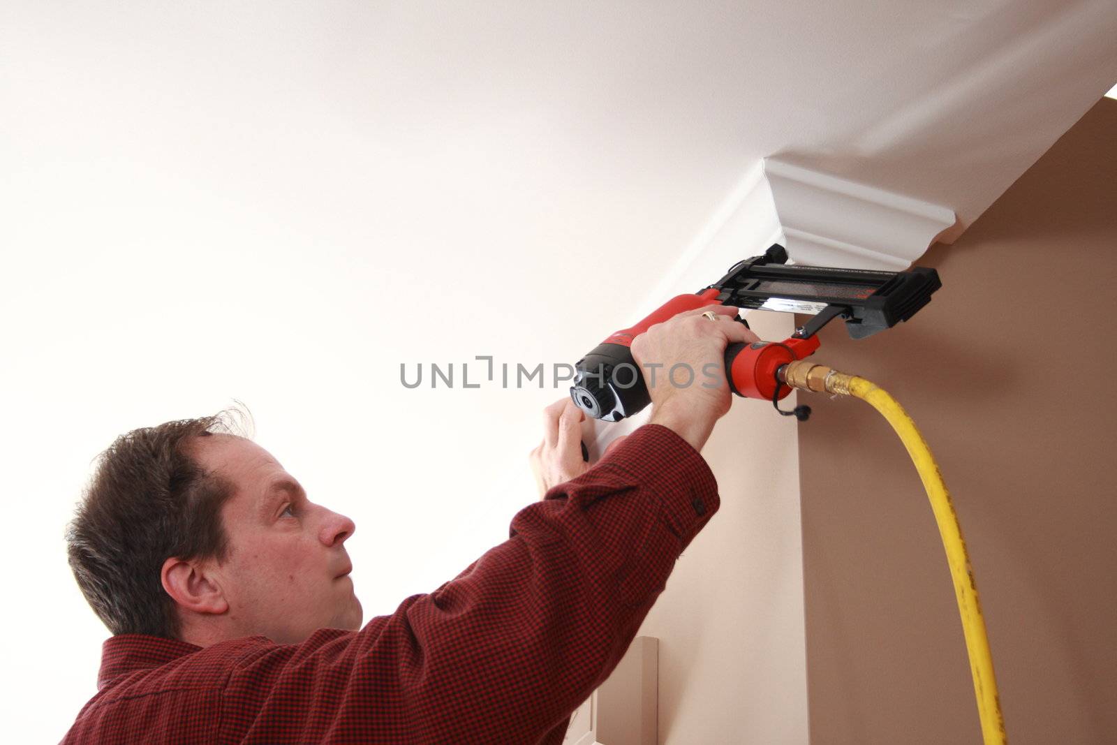 professional carpenter nailing crown moulding to wall during home improvement