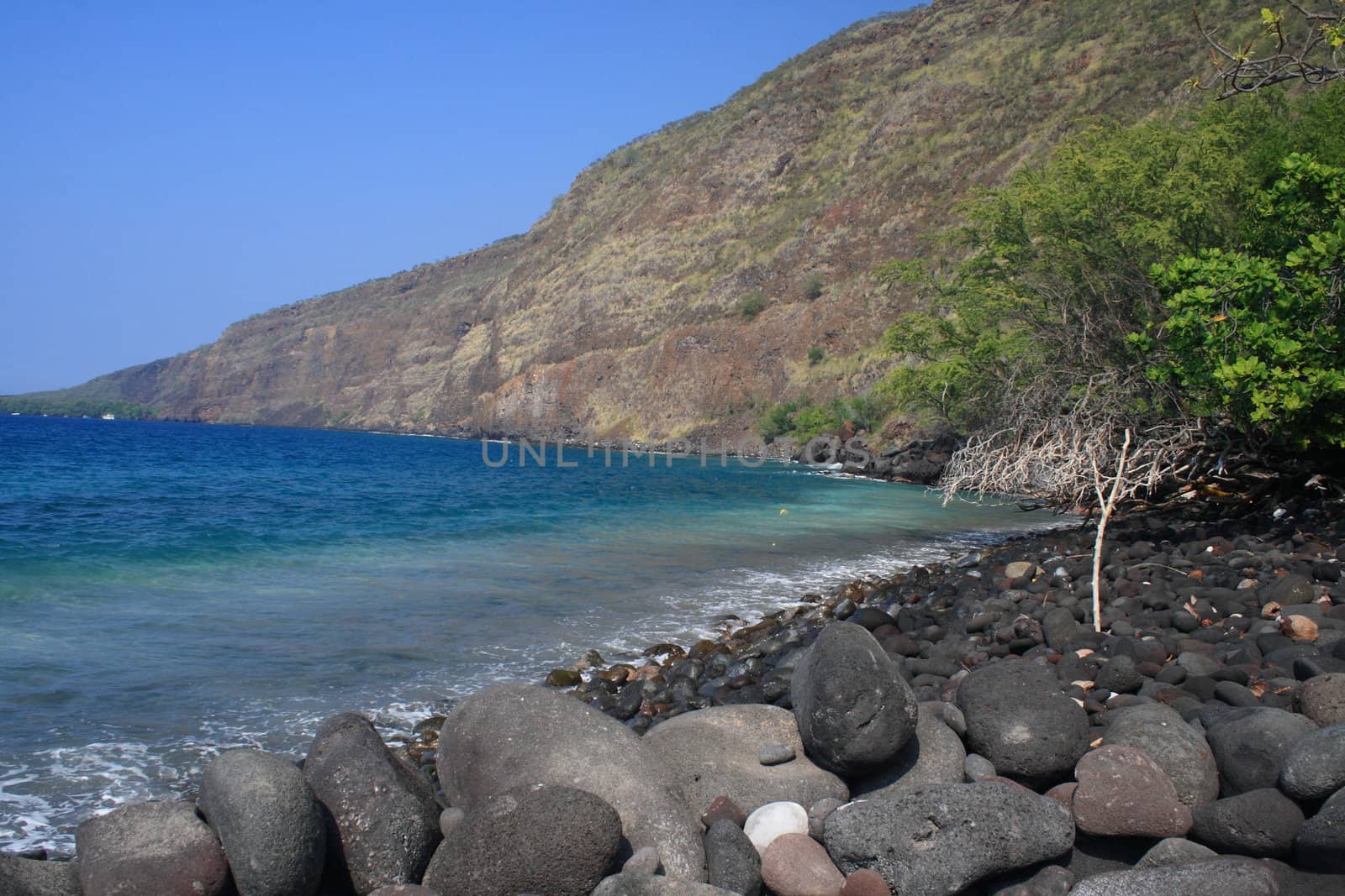 black rocks on an oceanside beach with a mountain in the background