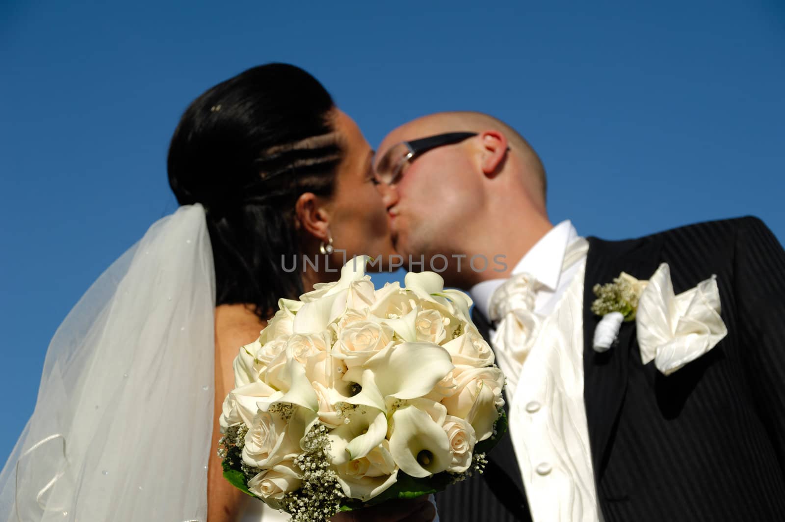 Bride and groom is kissing while showing their bouquet. Please note that the focus is on the flowers.