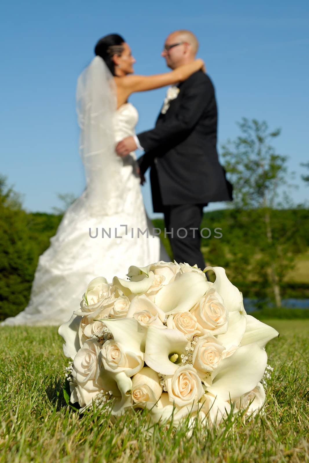 Wedding bouquet in grass in focus and wedding couple in the background.