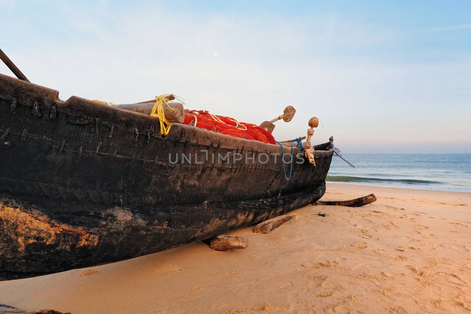 Old boat with fishing net on sandy shore. In Goa