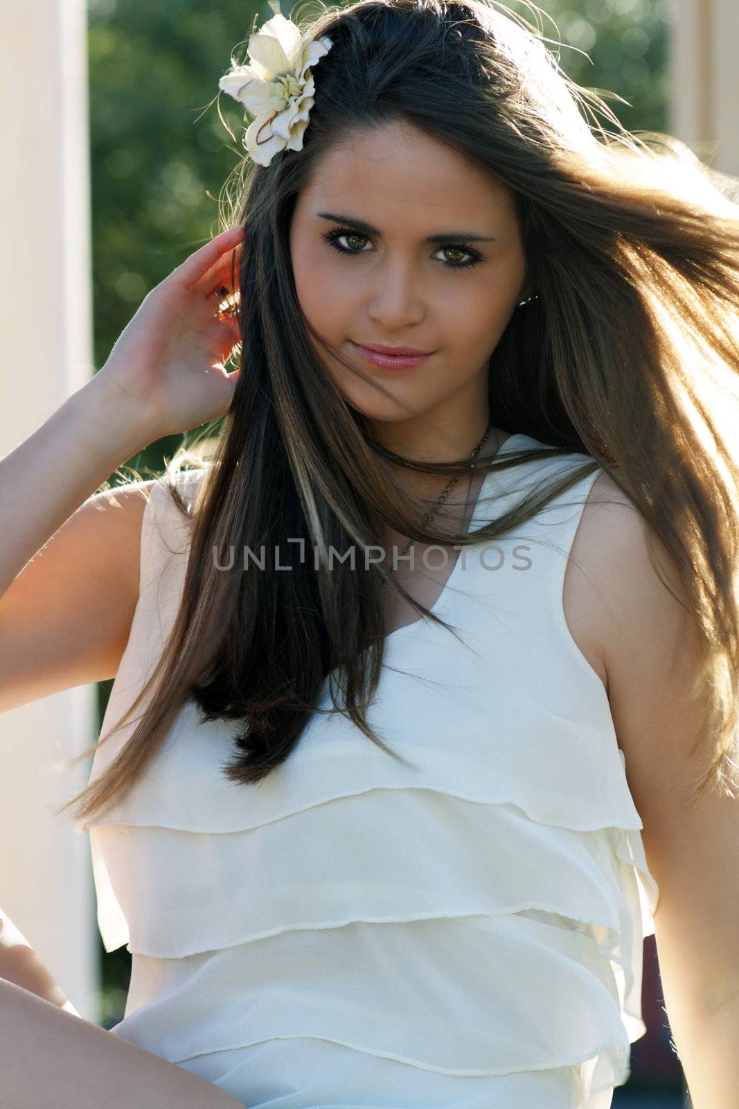 Close-up of a lovely young woman outdoors, backlit by the sun, looking directly at the camera.