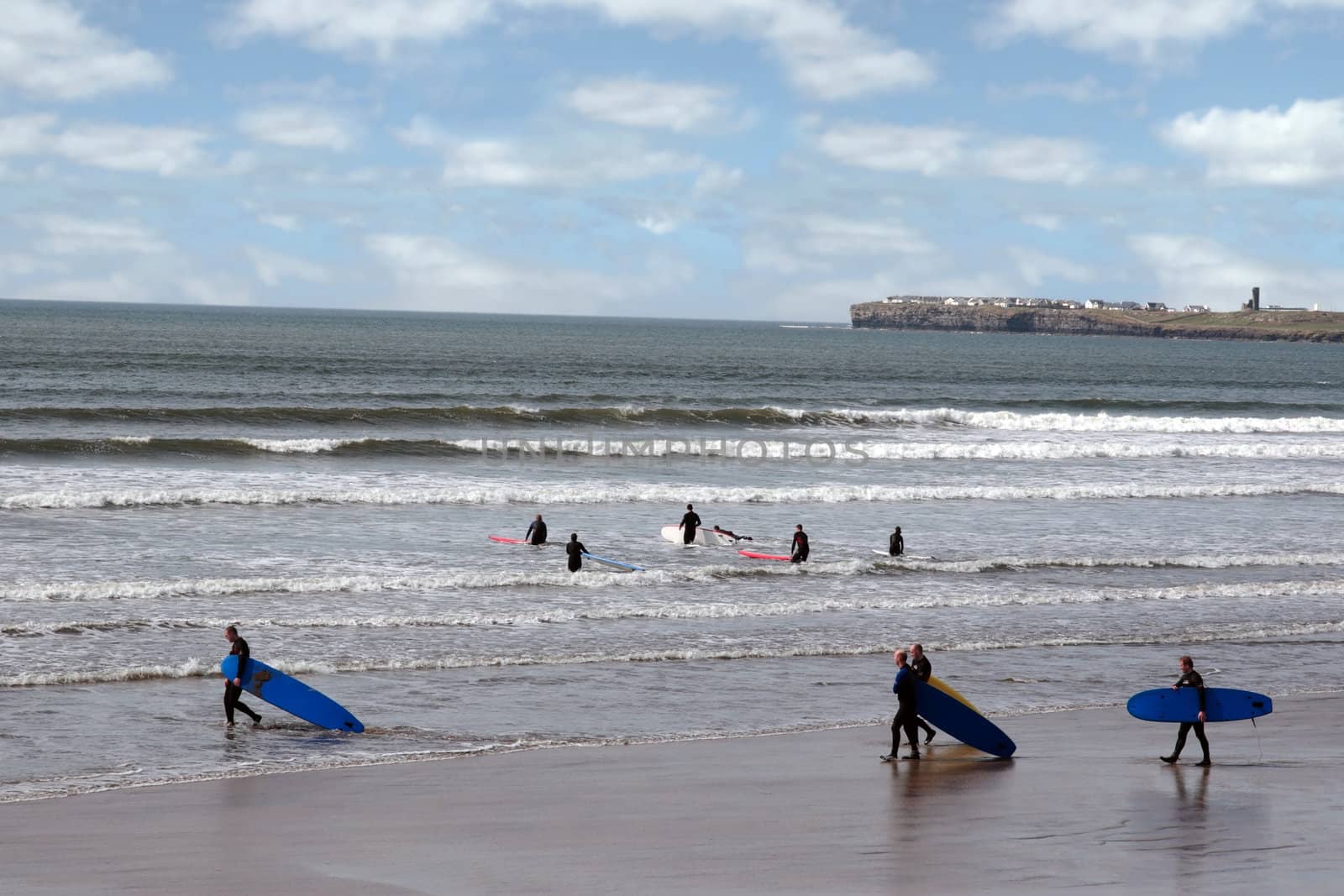 surfers walking on the beach in lahinch county clare ireland on a beautiful day