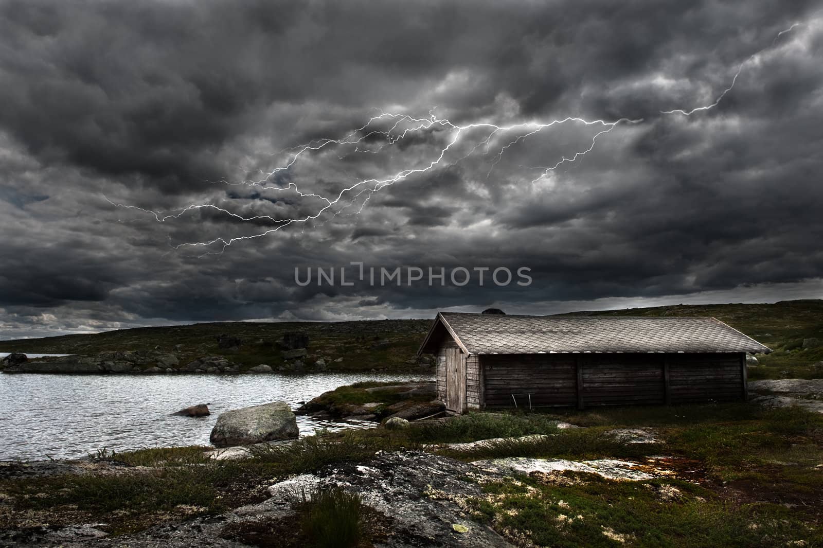 A lightning strikes over an old shed by a lake in the norwegian mountains
