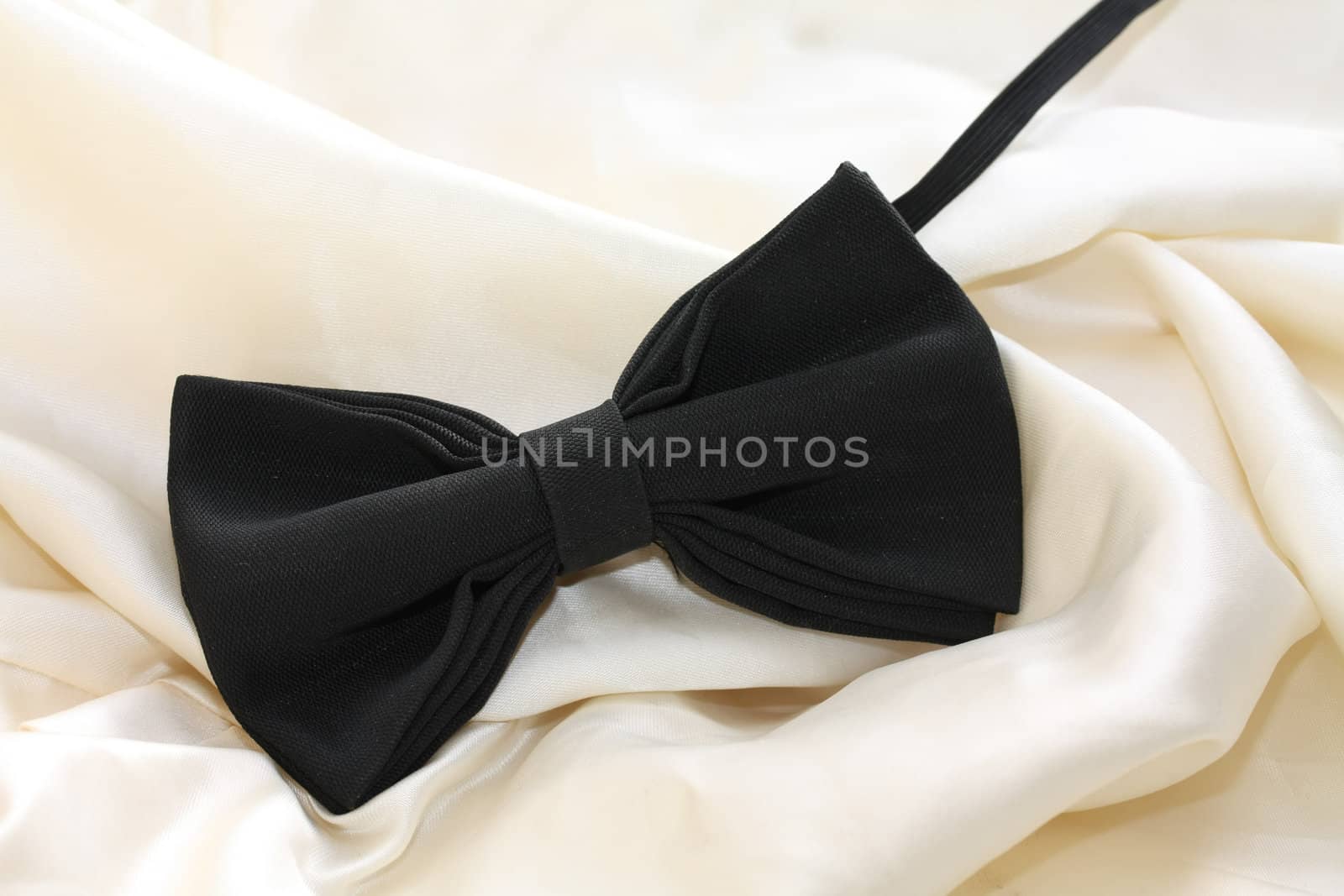 A black silk bow-tie on white satin, grooms accessory on his wedding day