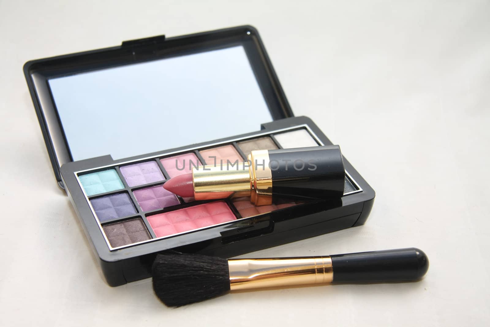 A palet with different shades of eye shadow, pink lipstick and a brush