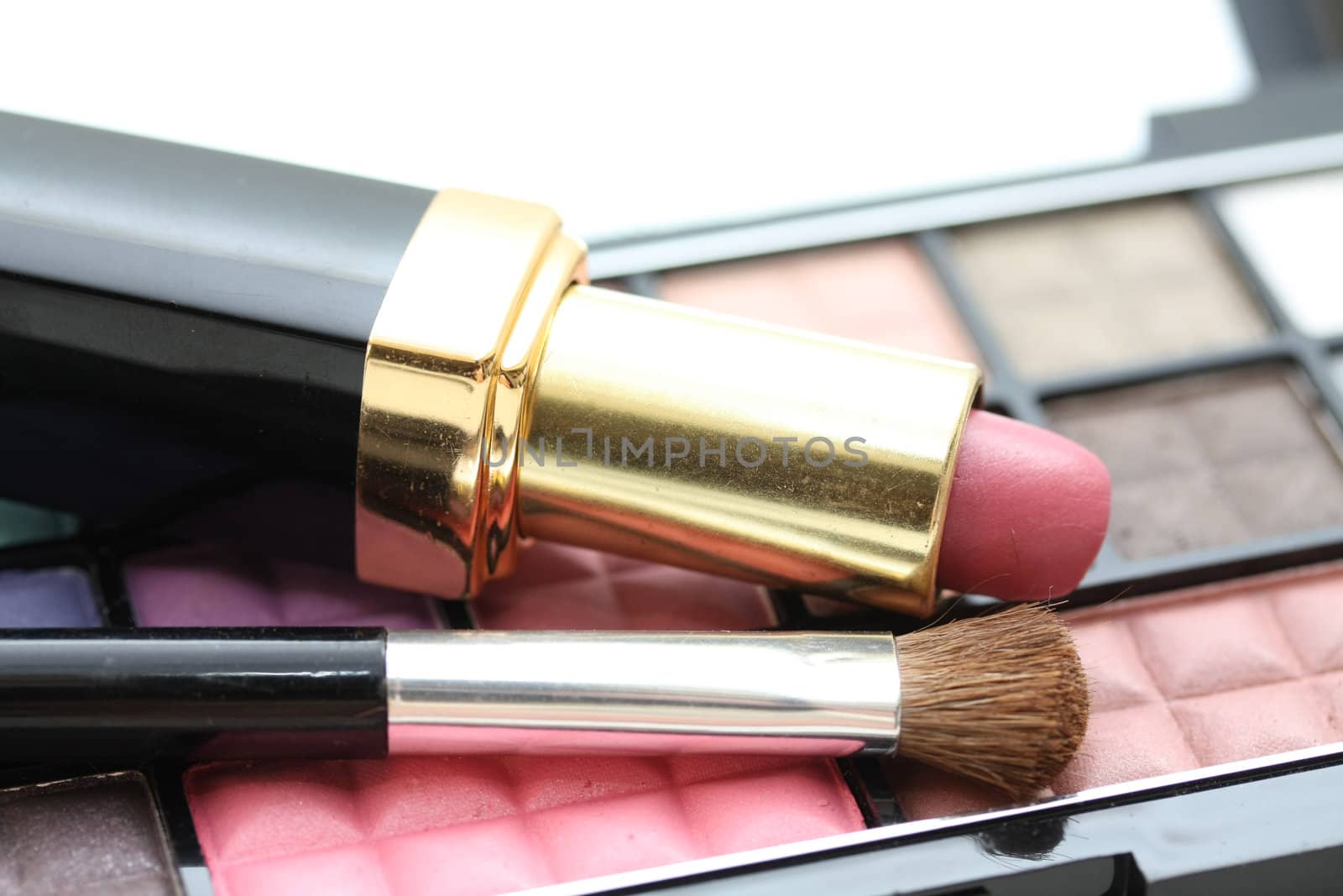 A palet with different shades of eye shadow, pink lipstick and a brush