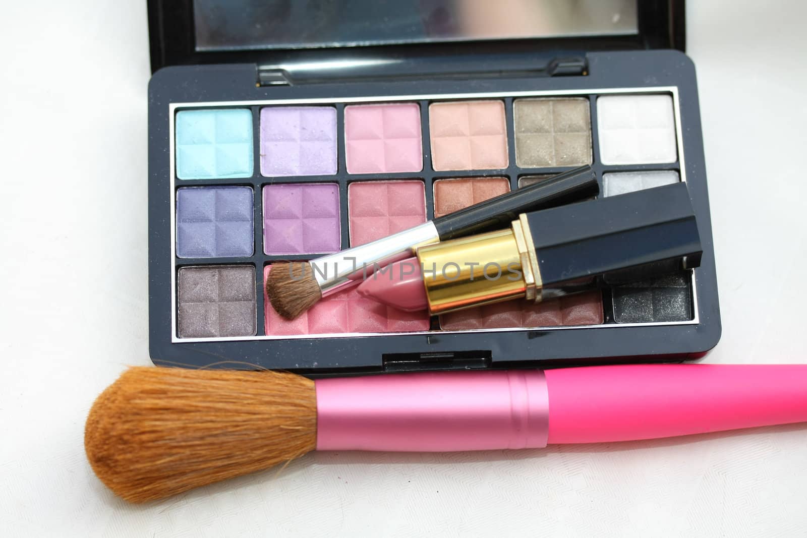 A palet with different shades of eye shadow, pink lipstick and a brush