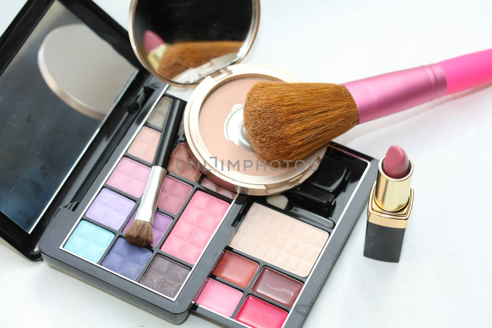 A palet with different shades of eye shadow, a compact powder, pink lipstick and a brush