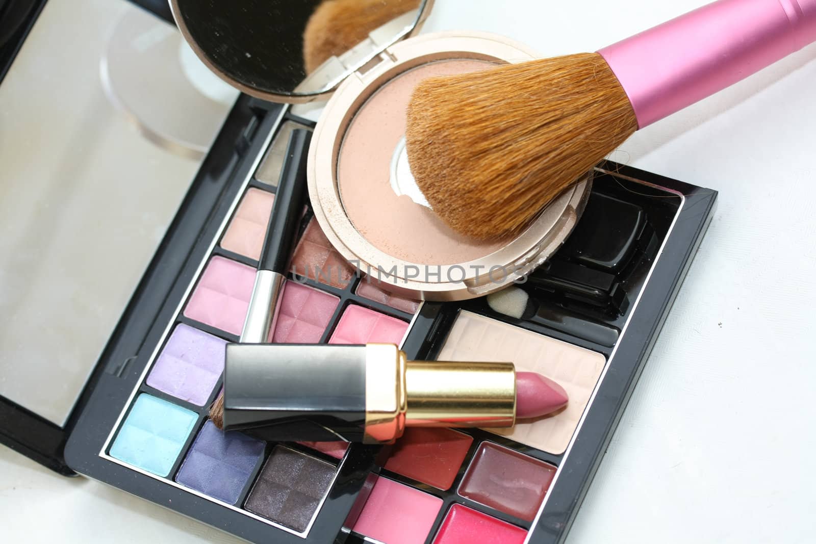 A palet with different shades of eye shadow, a compact powder, pink lipstick and a brush