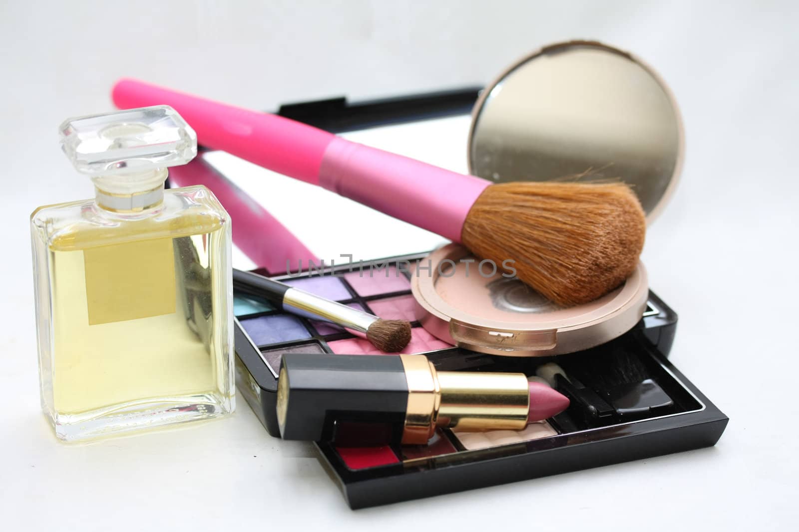 A palet with different shades of eye shadow, perfume bottle, a compact powder, pink lipstick and a brush