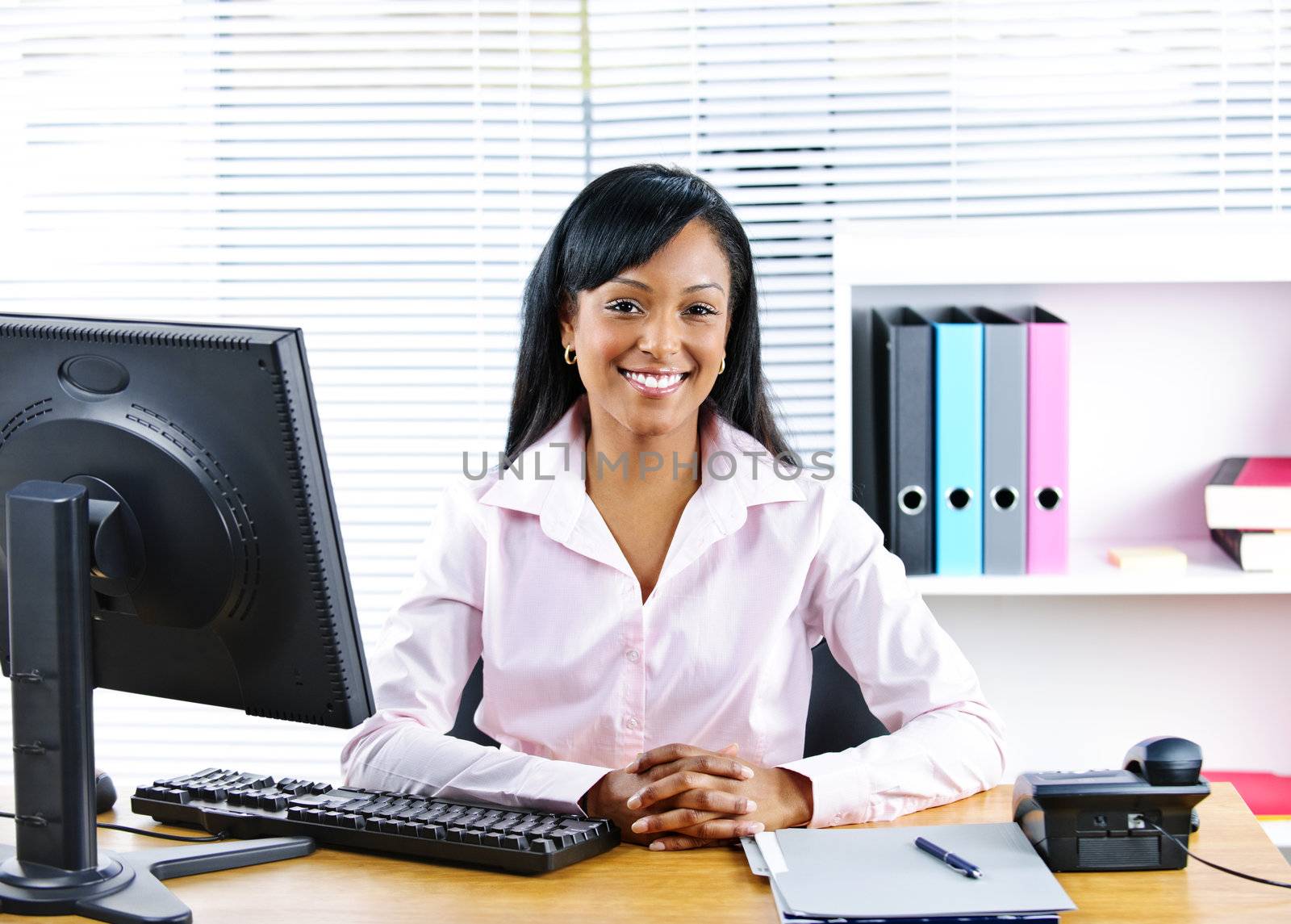 Portrait of smiling young black business woman at desk in office