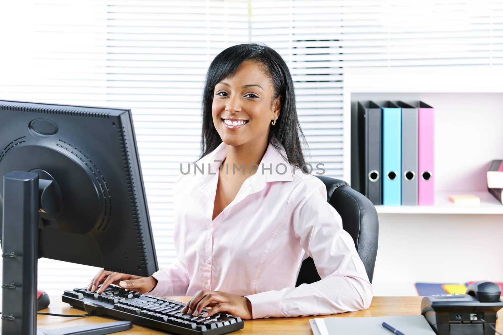 Portrait of happy black business woman at desk typing on computer