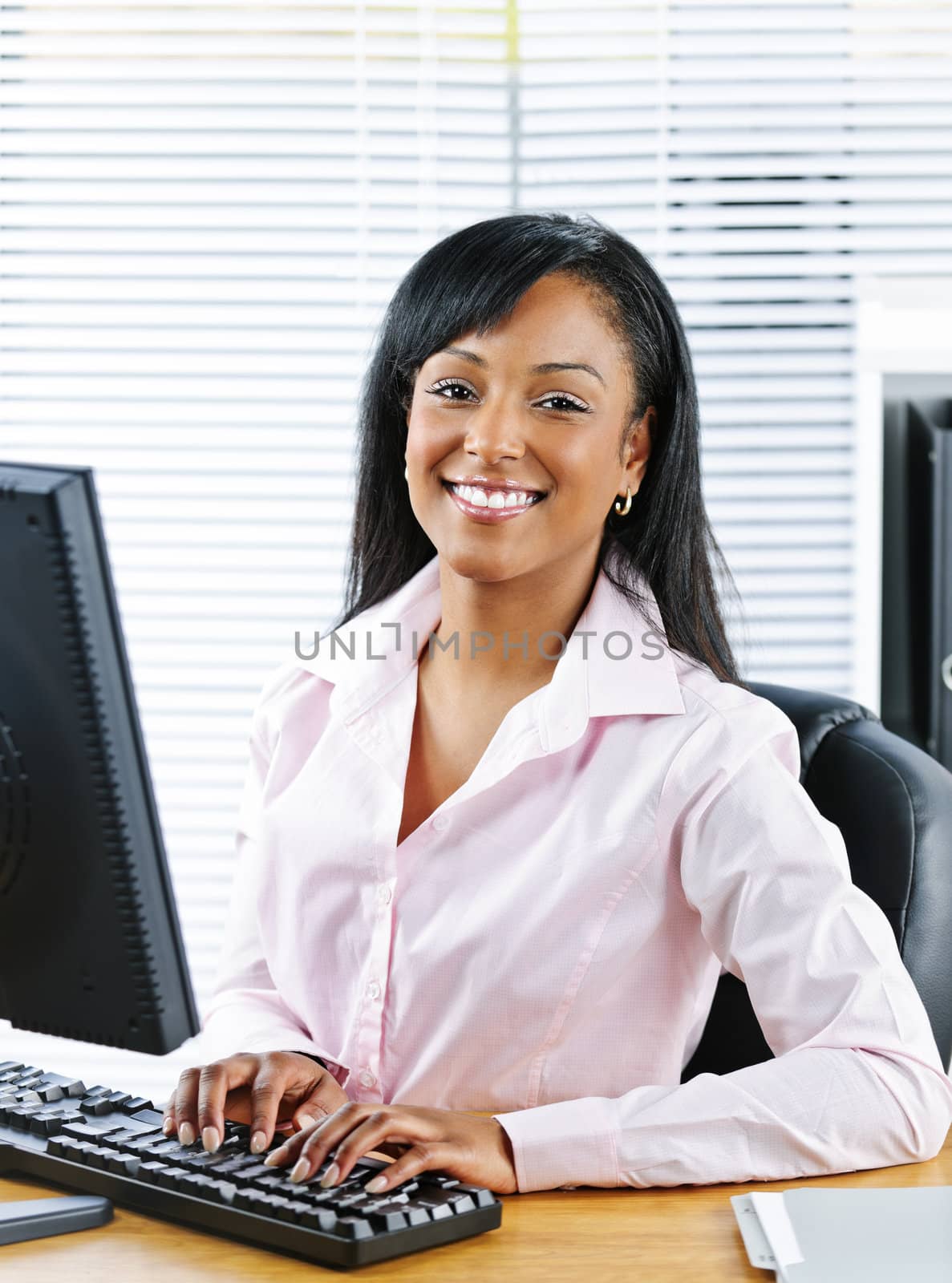 Portrait of young smiling black business woman at desk typing on computer