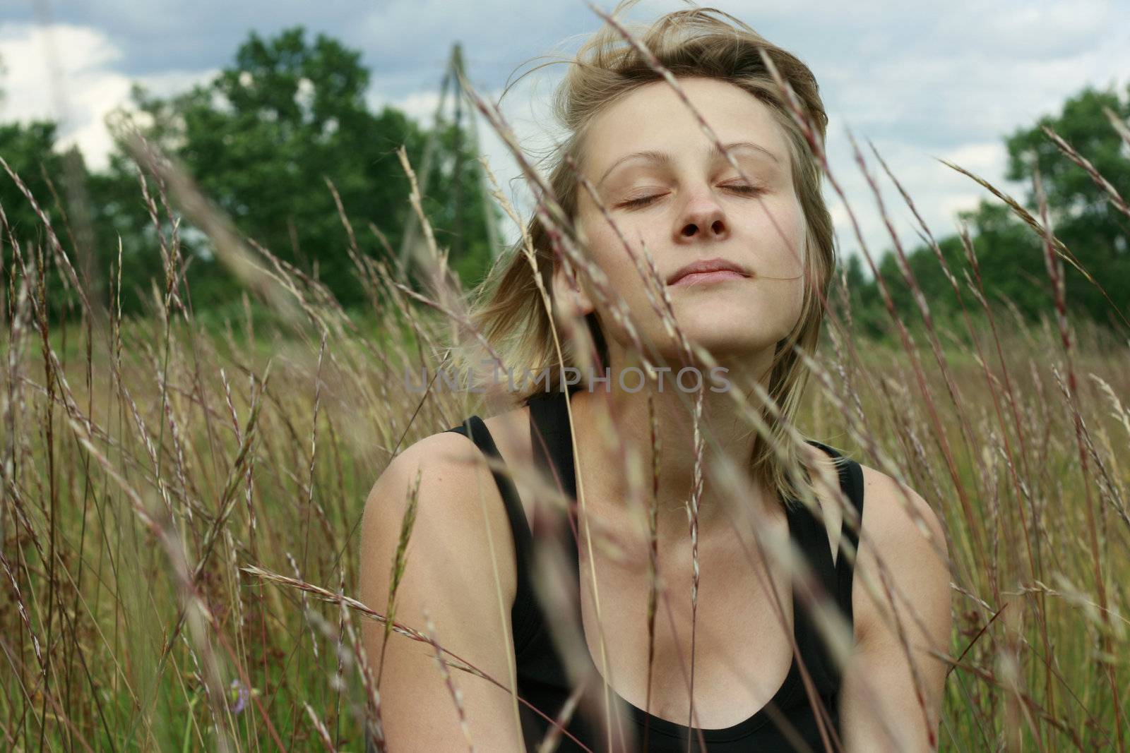 Young woman sitting in meadow and enjoying summer wind with closed eyes.