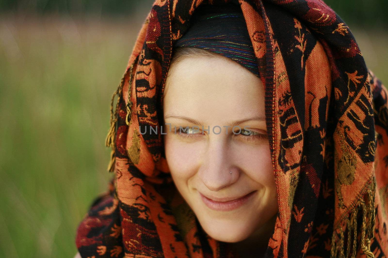 Young woman with traditional kerchief over head sitting in meadow and and smiling.