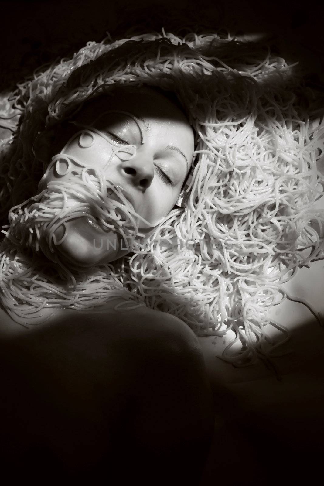 lack and white photo of woman laying on ground with spaghetti all over around the head.