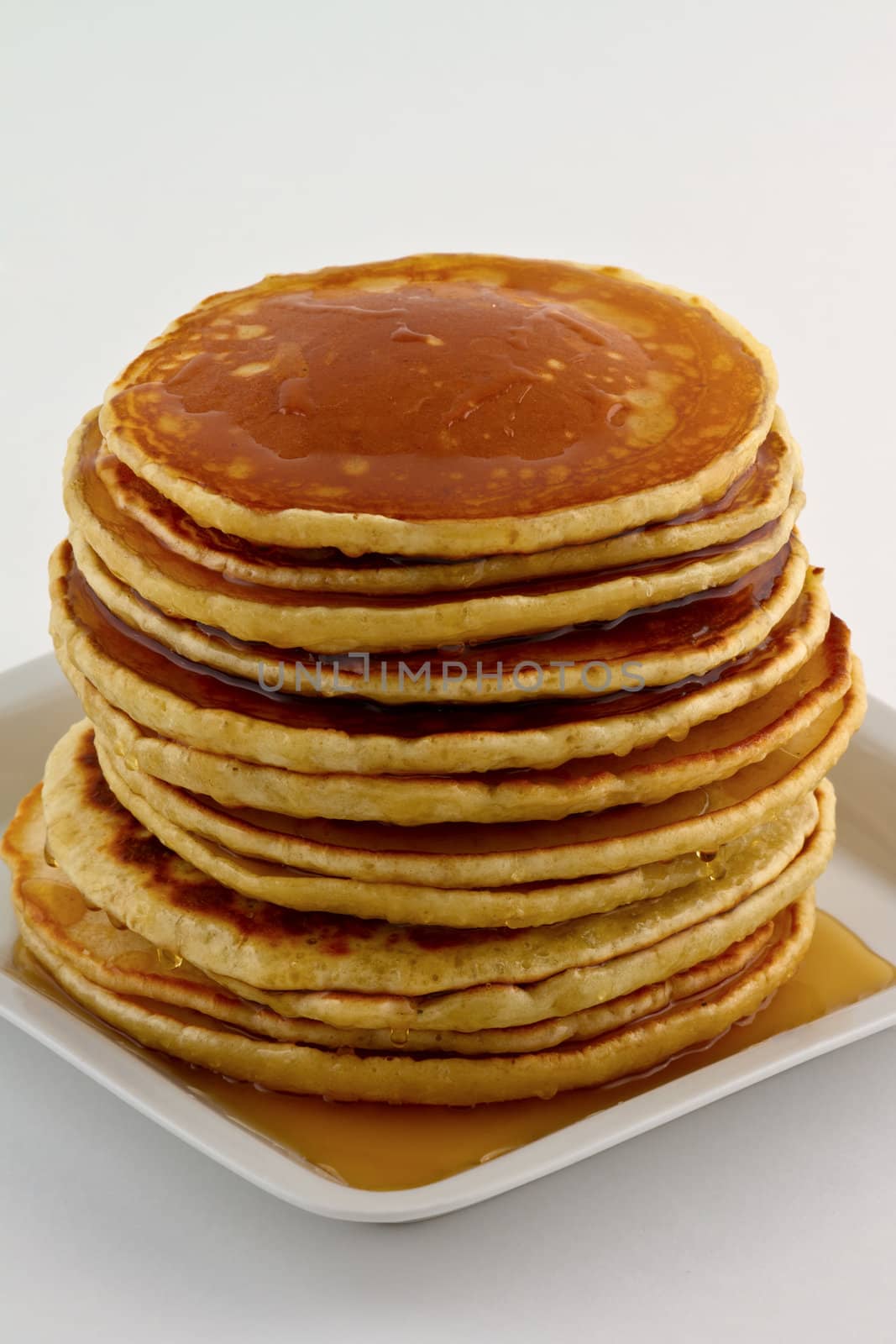 Stack of homemade pancakes with syrup on a white plate.