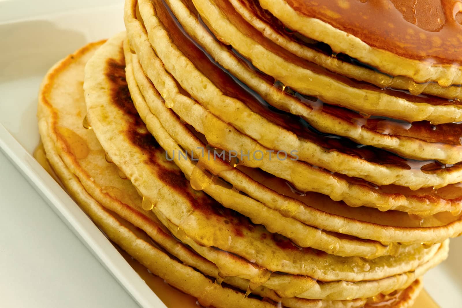 Stack of homemade pancakes with syrup on a white plate.