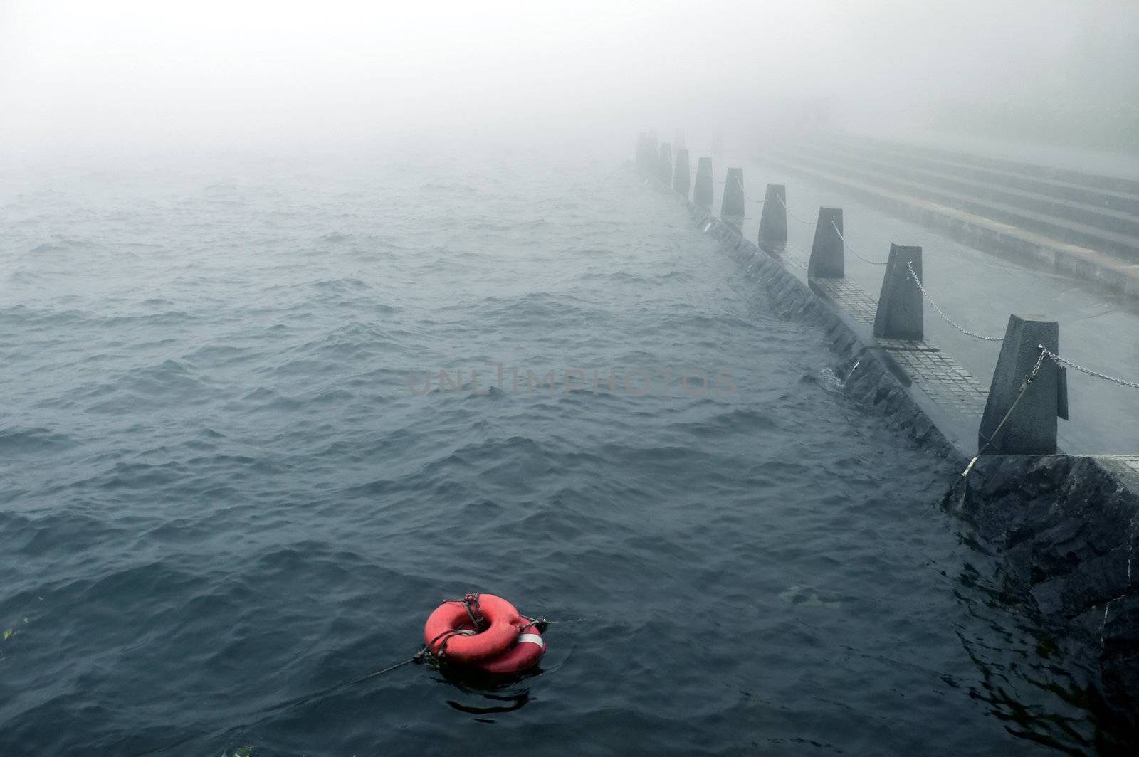 bad weather with mist on the embankment with redlife-buoy on the water