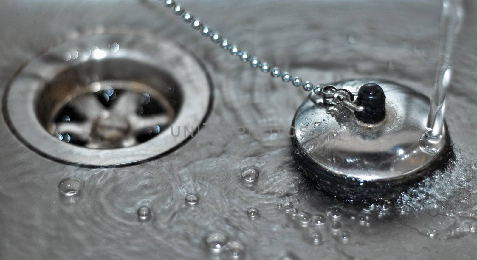 Macro shot of a plug in a sink with running water and water bubbles