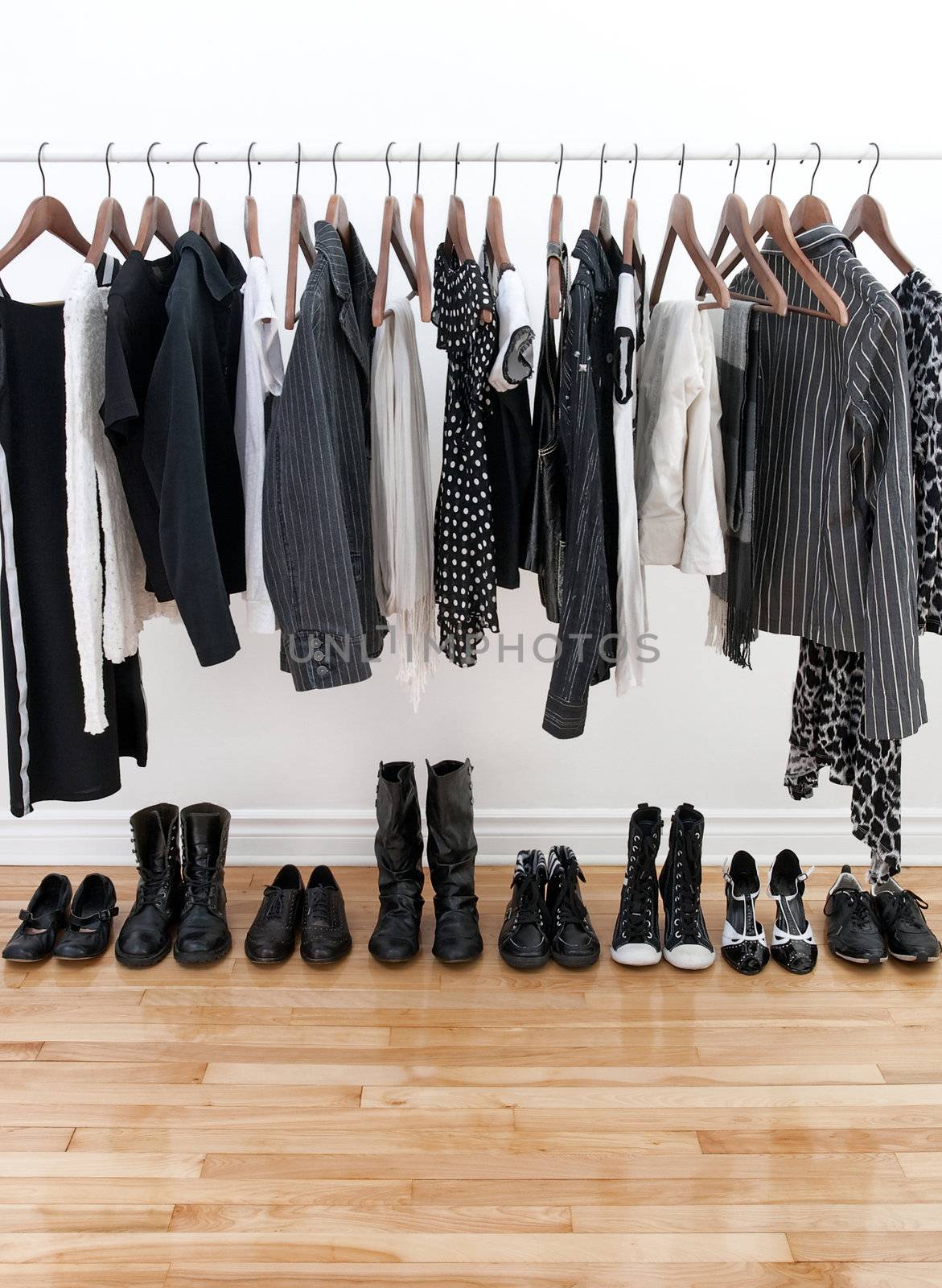 Black and white female clothes on hangers and shoes on a wooden floor.