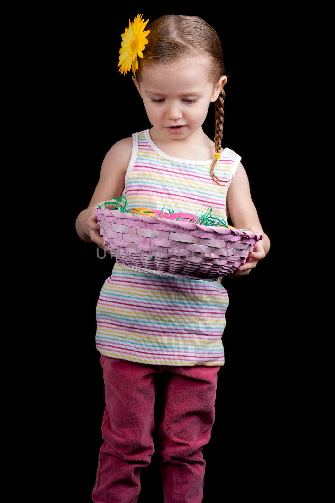 A beautiful young child looks in her pink easter basket.  She could be counting her eggs before there hatched!