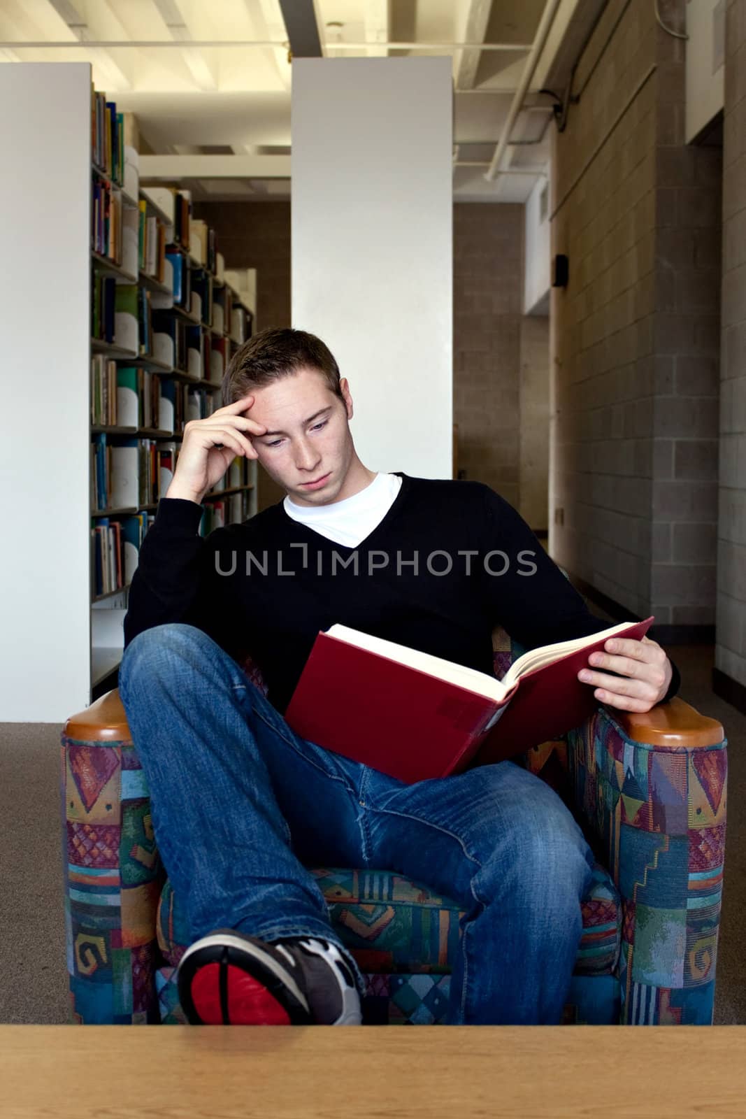 A young college aged man reading a book at the library.