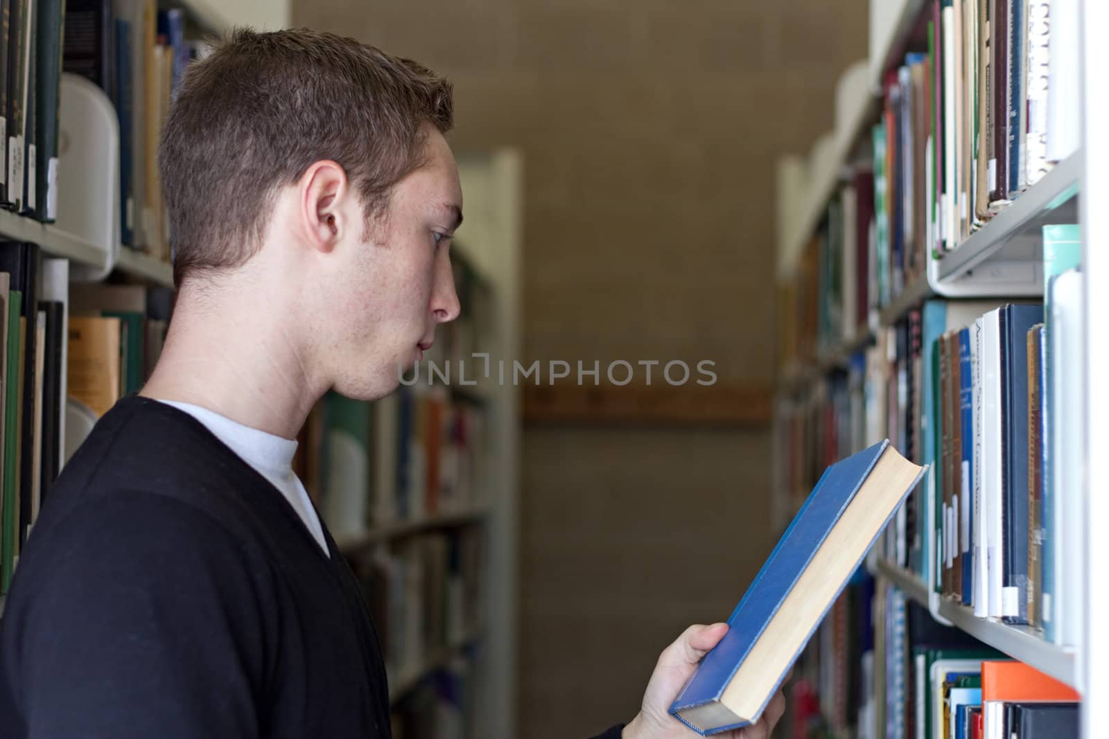 A young college aged man look at a book at the library.