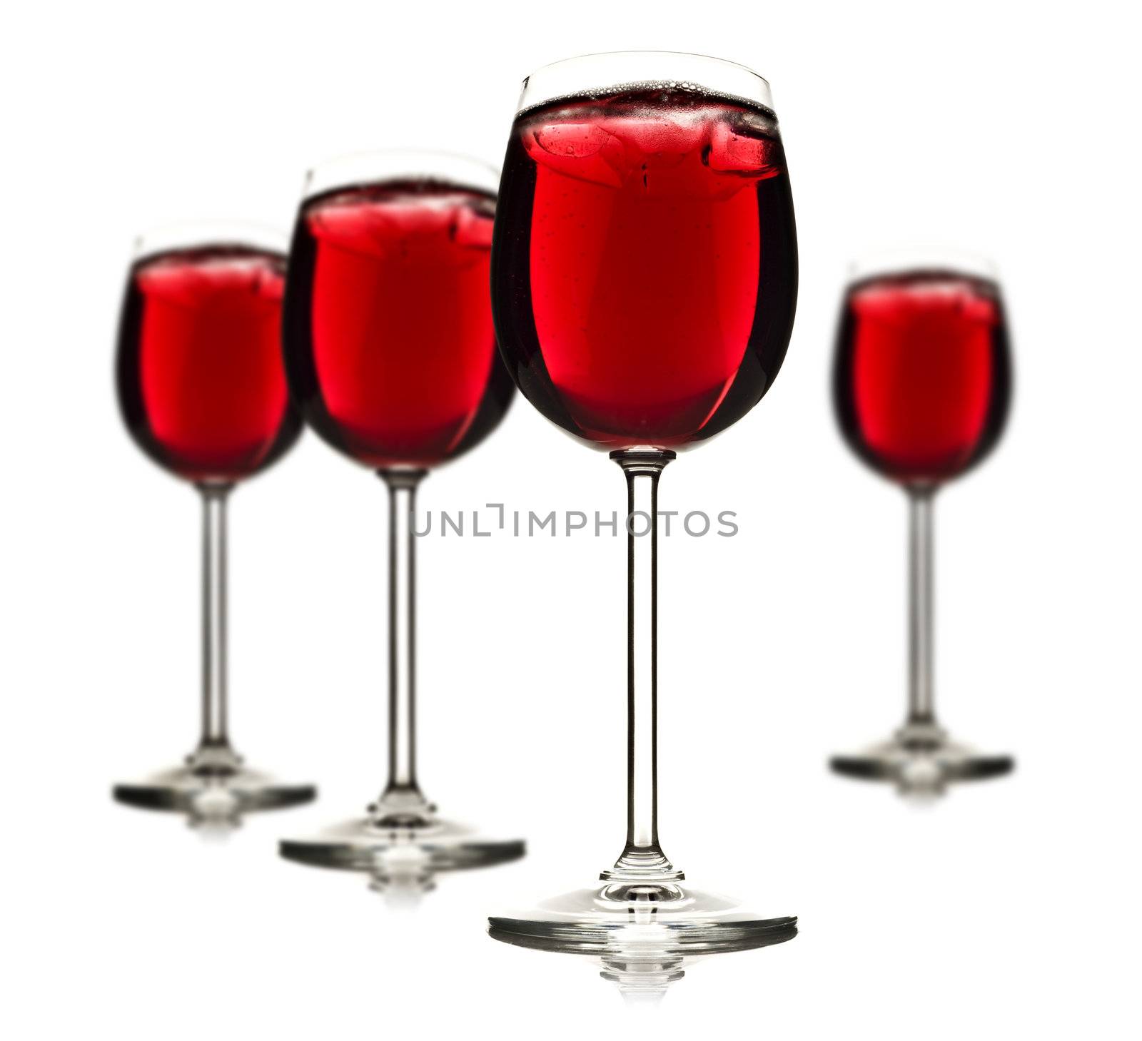 Four wine glasses with red fruit juice and ice on a white background