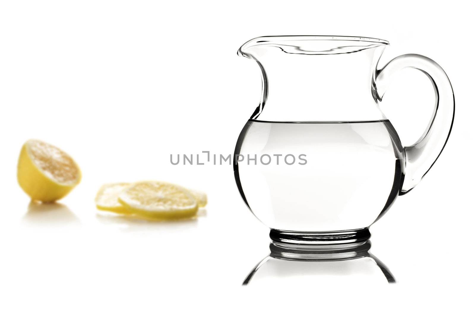 Glass pitcher with water and lemon slices on white