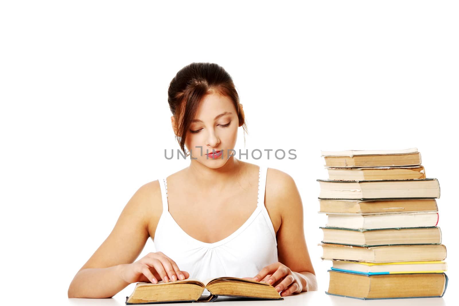 Young pretty caucasain girl sitting and reading a book near pile of books.