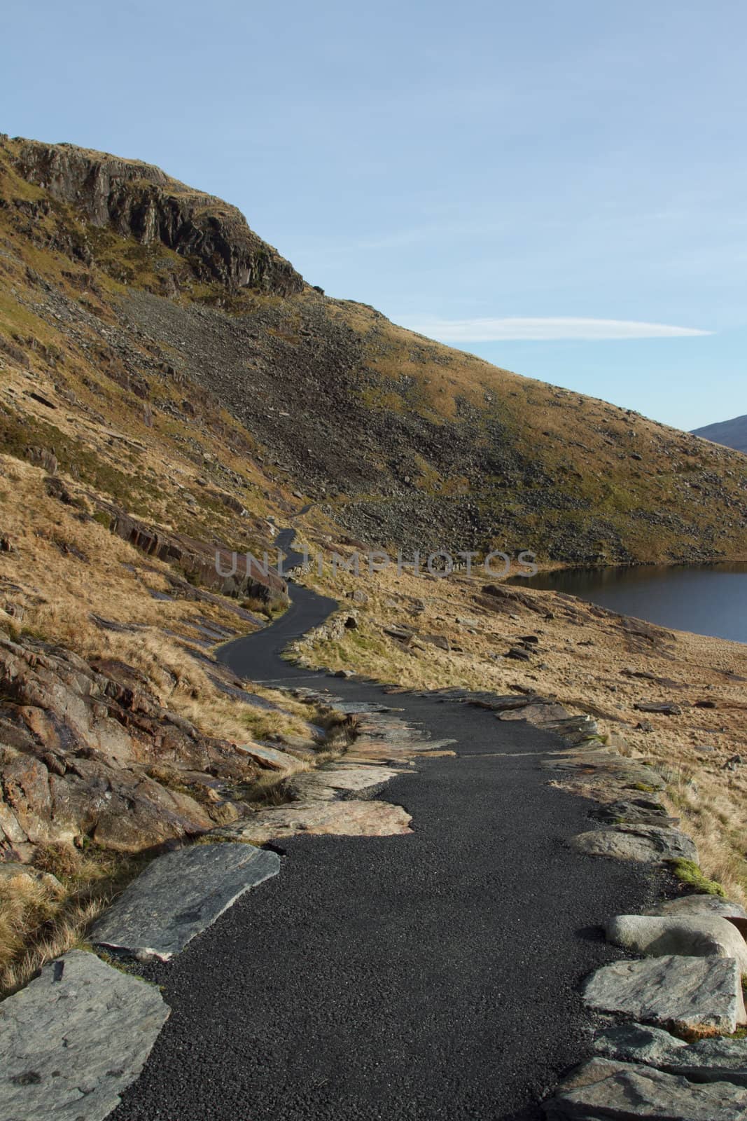 A tarmac footpath weaves through and contours around a hillside with rocks and grass.