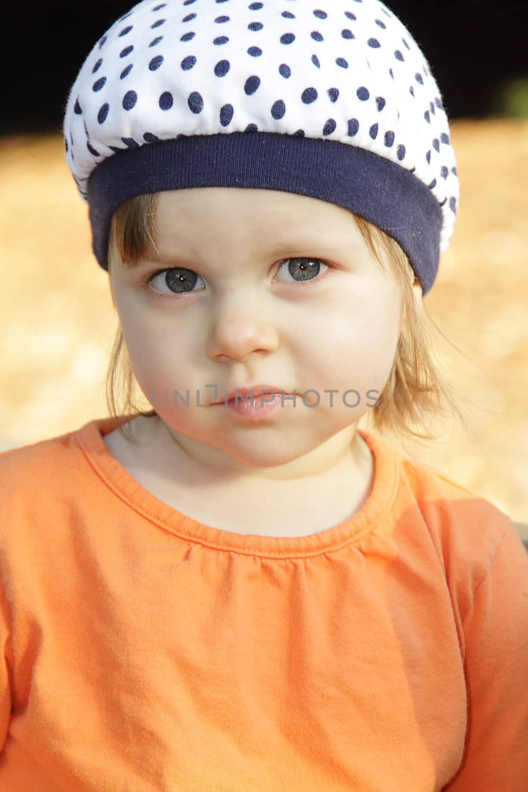 Cute little girl in orange shirt and white hat outdoors