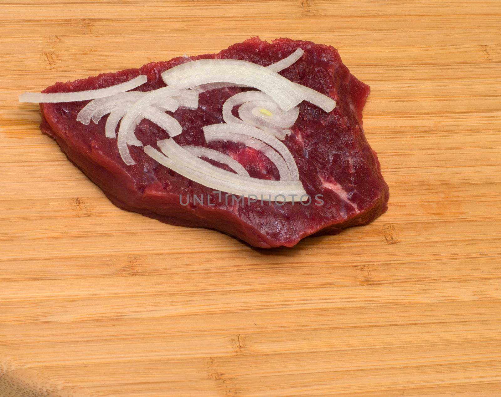 A piece of beef and onions on a cutting board.